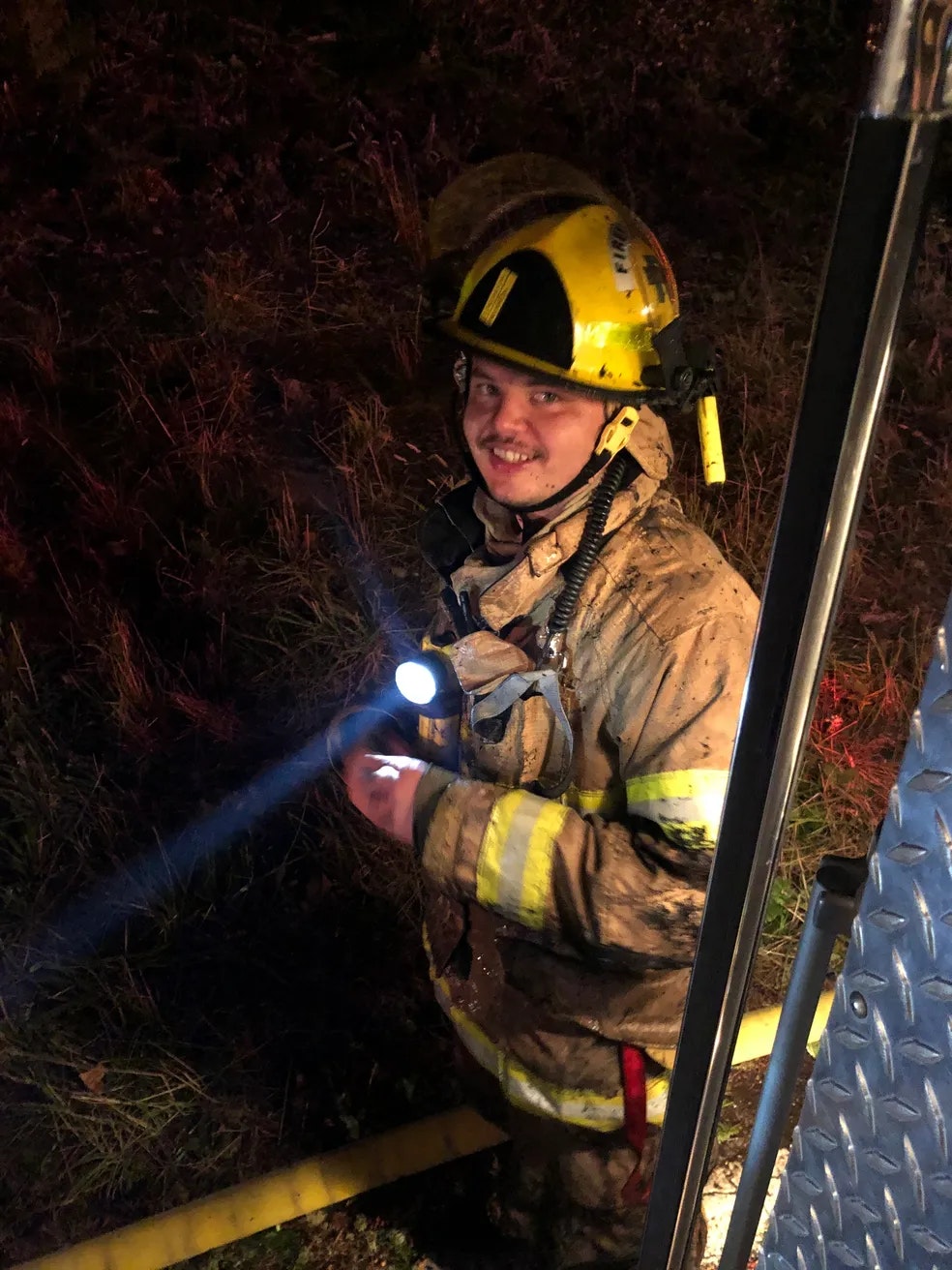 Firefighter using a flashlight at night near a burning area.