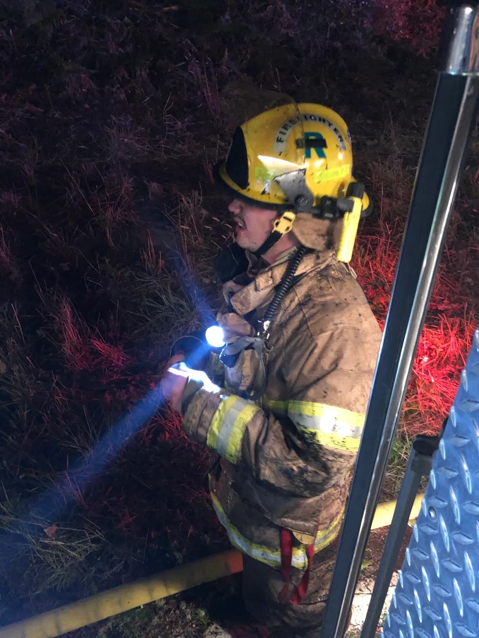 Firefighter illuminated at night, holding a fire hose.