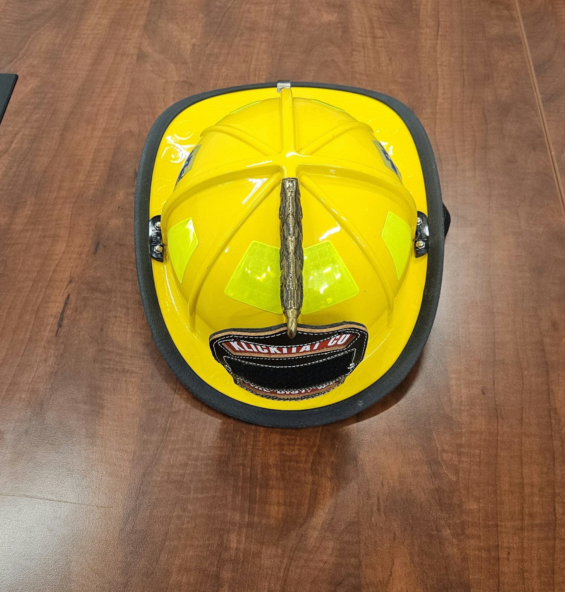 A yellow firefighter helmet on a wooden table with a badge and reflective strips.