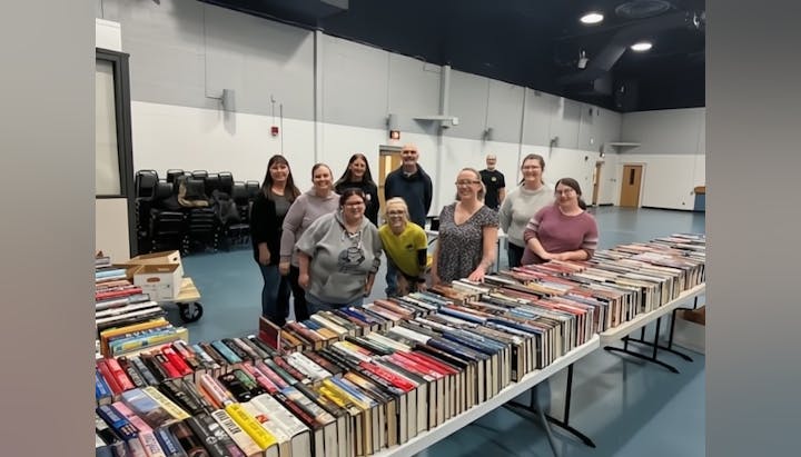A group of people standing behind tables filled with books, set up indoors.