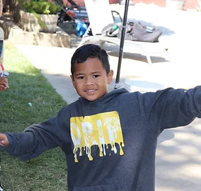 A child in a hoodie with a "DRIP" print, standing outside with arms wide open, smiling.