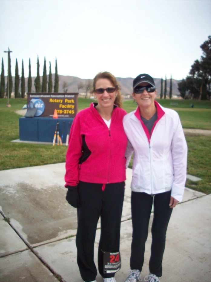 Two people in athletic gear posing in front of a park sign.