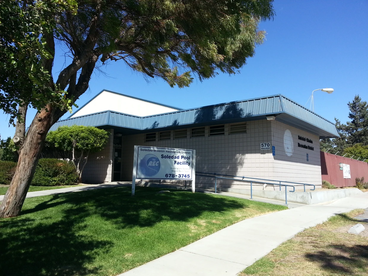 Public pool facility with a sign, trees, and blue sky.