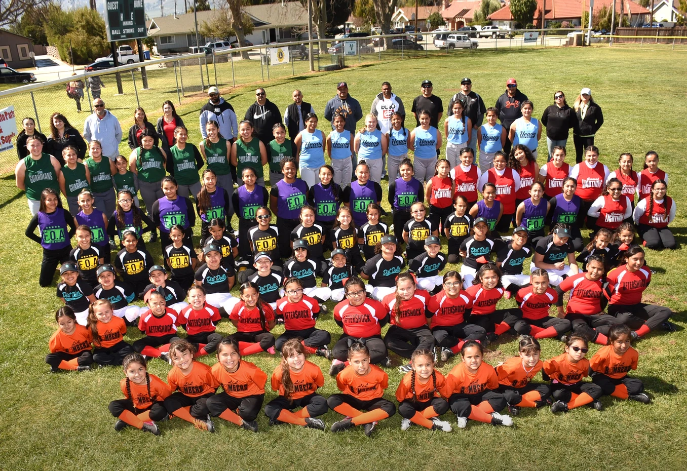 Group of young athletes in colorful uniforms with coaches, posing on a sports field.