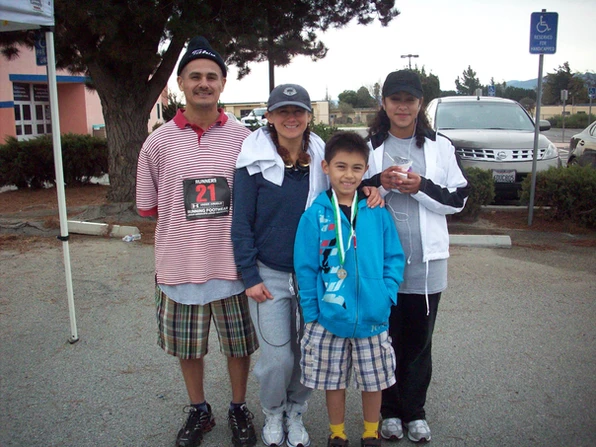 Four people posing together, one with a medal, in a parking lot.