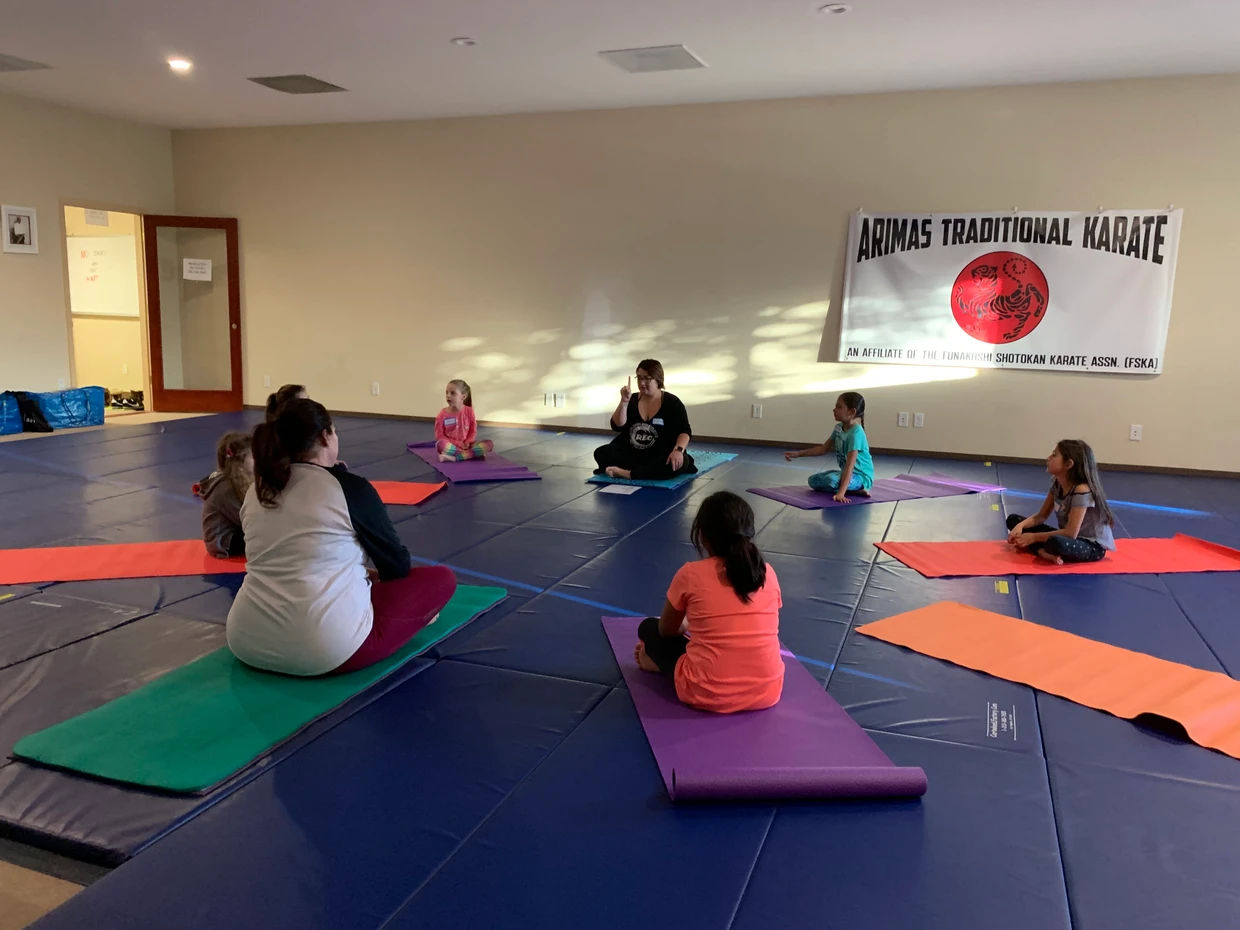 Group sitting on mats in a karate dojo with a banner on the wall.