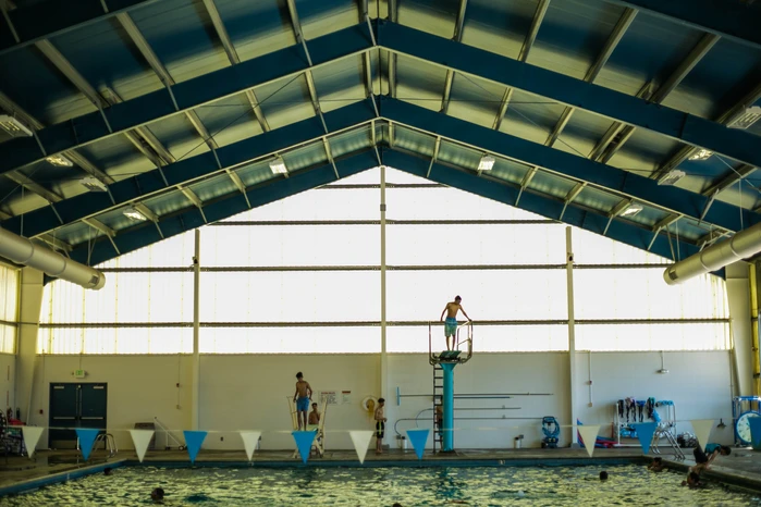 Indoor swimming pool with divers, swimmers, and large windows.