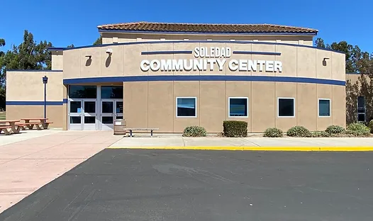 A building labeled "Soledad Community Center" with a clear blue sky and ample parking in front.