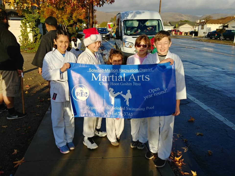 A group of kids in martial arts uniforms holding a "Martial Arts" banner outdoors.