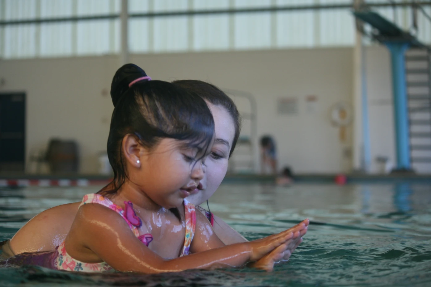 Adult teaches child to swim in an indoor pool.