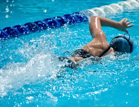 A swimmer wearing a cap is doing the freestyle stroke in a pool with lane dividers.