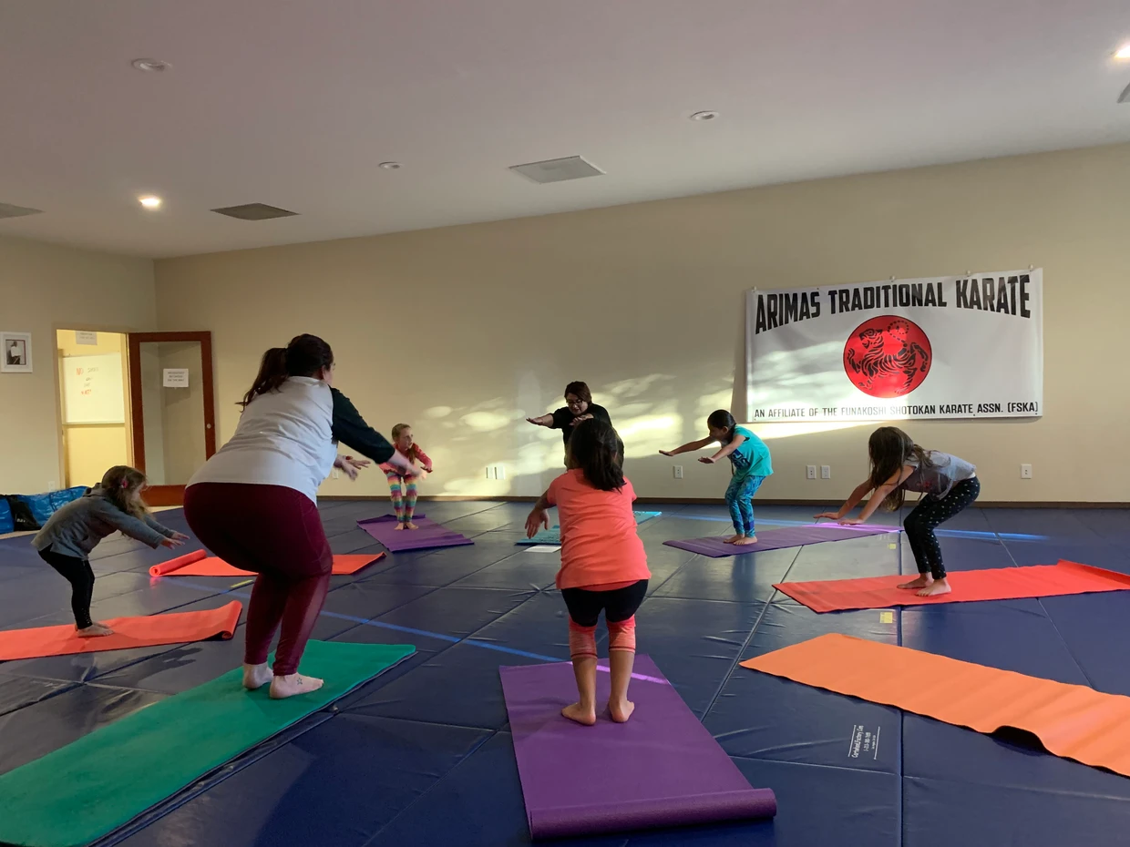 A group of people, including children, practicing yoga in a room with karate dojo banners.