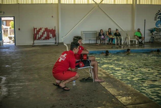 Two lifeguards watching over a swimming pool, with people in the background.