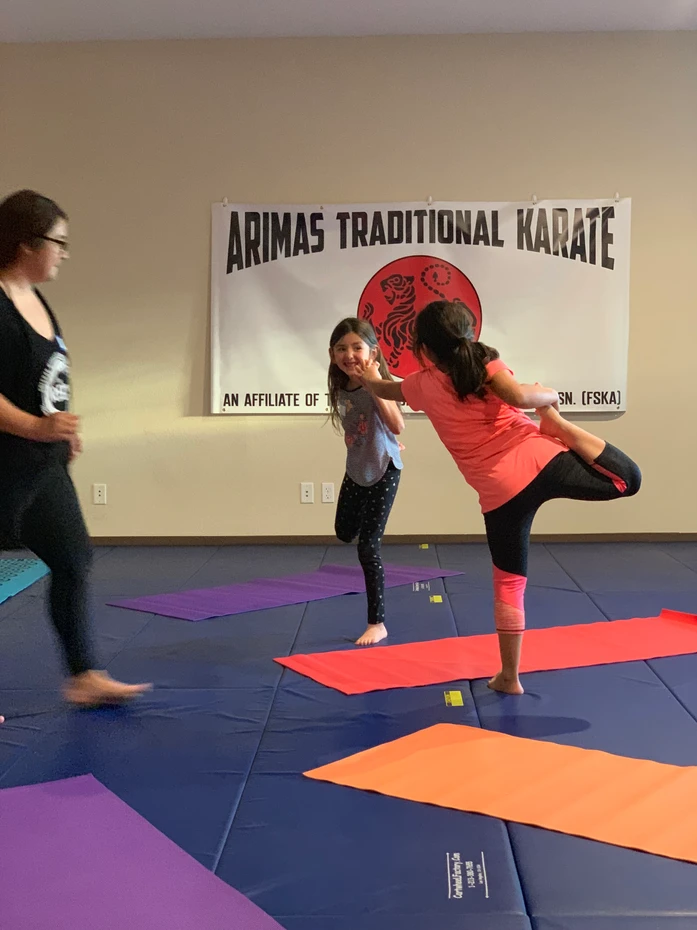 Children practicing karate in a dojo with mats on the floor and a banner in the background.
