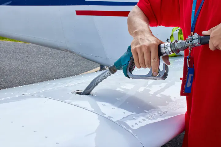 Person refueling an aircraft by inserting a hose into the wing's fuel tank inlet.