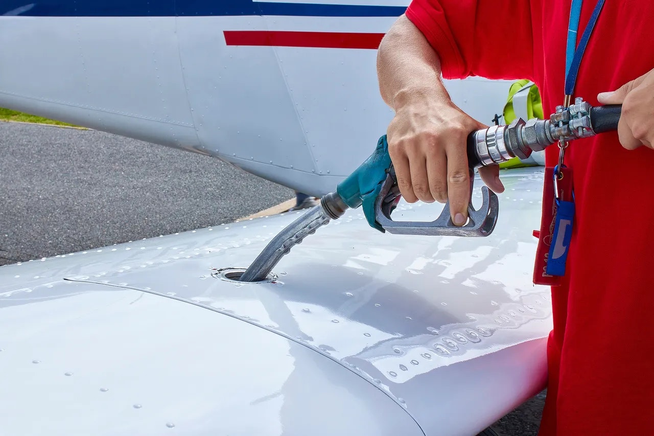 Person refueling an aircraft by inserting a hose into the wing's fuel tank inlet.