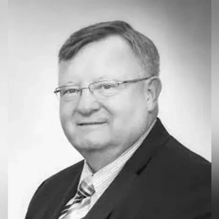 A grayscale portrait of a middle-aged man in a suit and tie, smiling slightly.