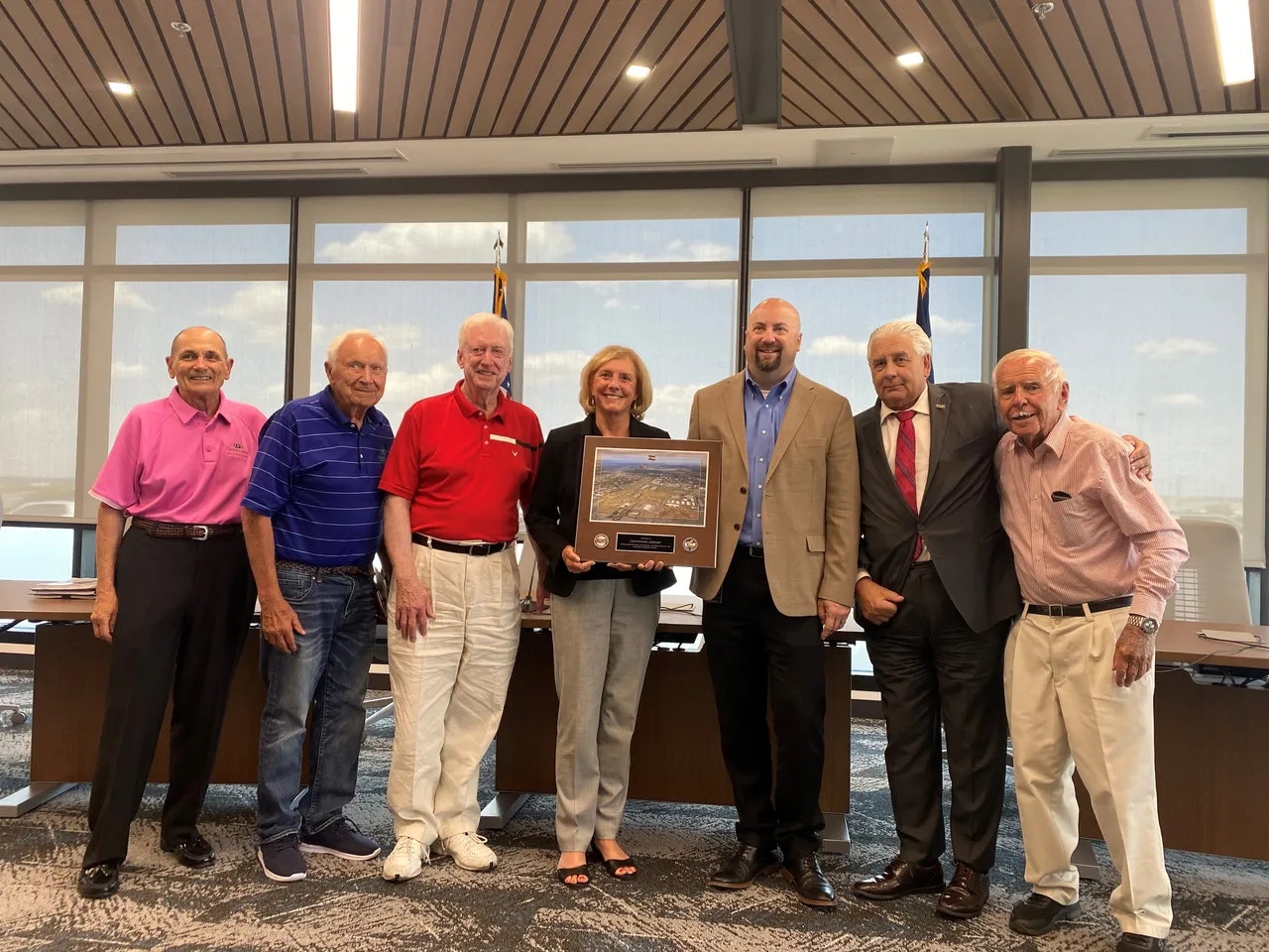 A group of people posing indoors, one holding a framed picture.