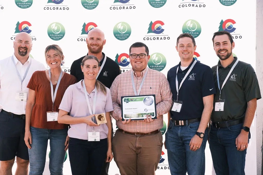 A group of seven people smiling, two holding awards, in front of a Colorado-themed backdrop.