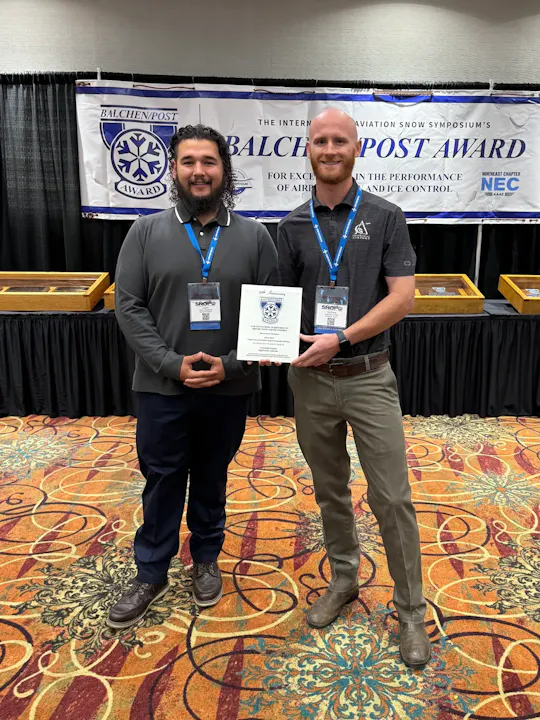 Two people standing with an award at the Balchen/Post Award ceremony, related to airport snow and ice control.