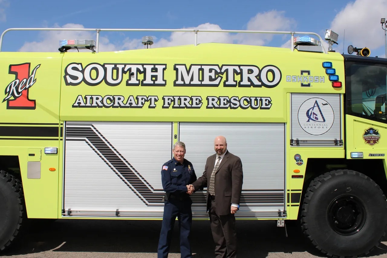 Two people shaking hands in front of a "South Metro Aircraft Fire Rescue" truck.