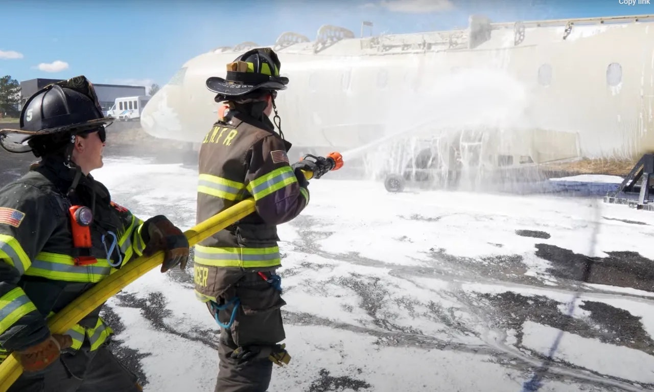 Firefighters spraying foam on a plane during a training exercise.
