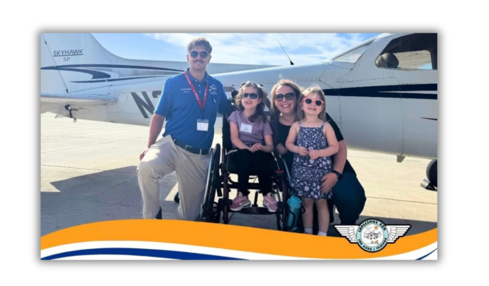 A group of four people, including two young girls, poses by a small airplane, smiling and wearing sunglasses.
