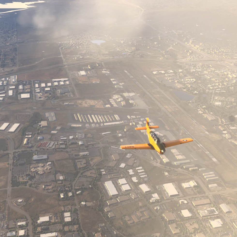 An orange aircraft flying above an industrial landscape with runways, buildings, and some clouds in the sky.