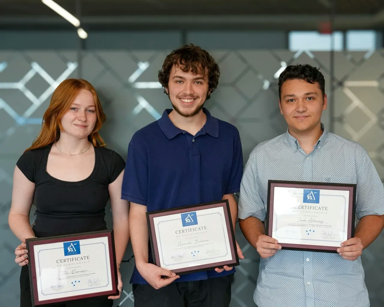 Three people holding certificates, standing and smiling.