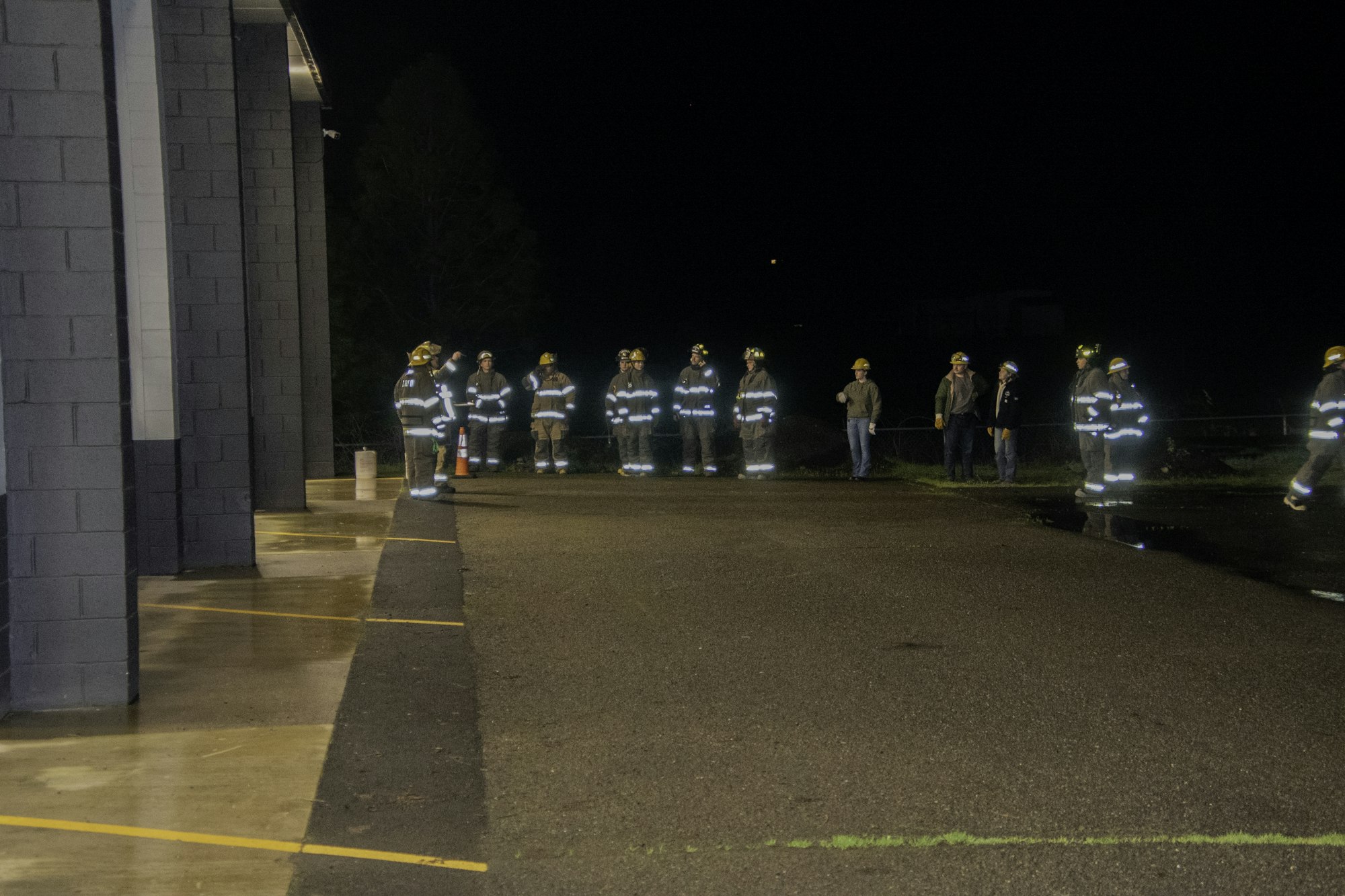 Firefighters and others are gathered outside a building at night, possibly for training or an event.