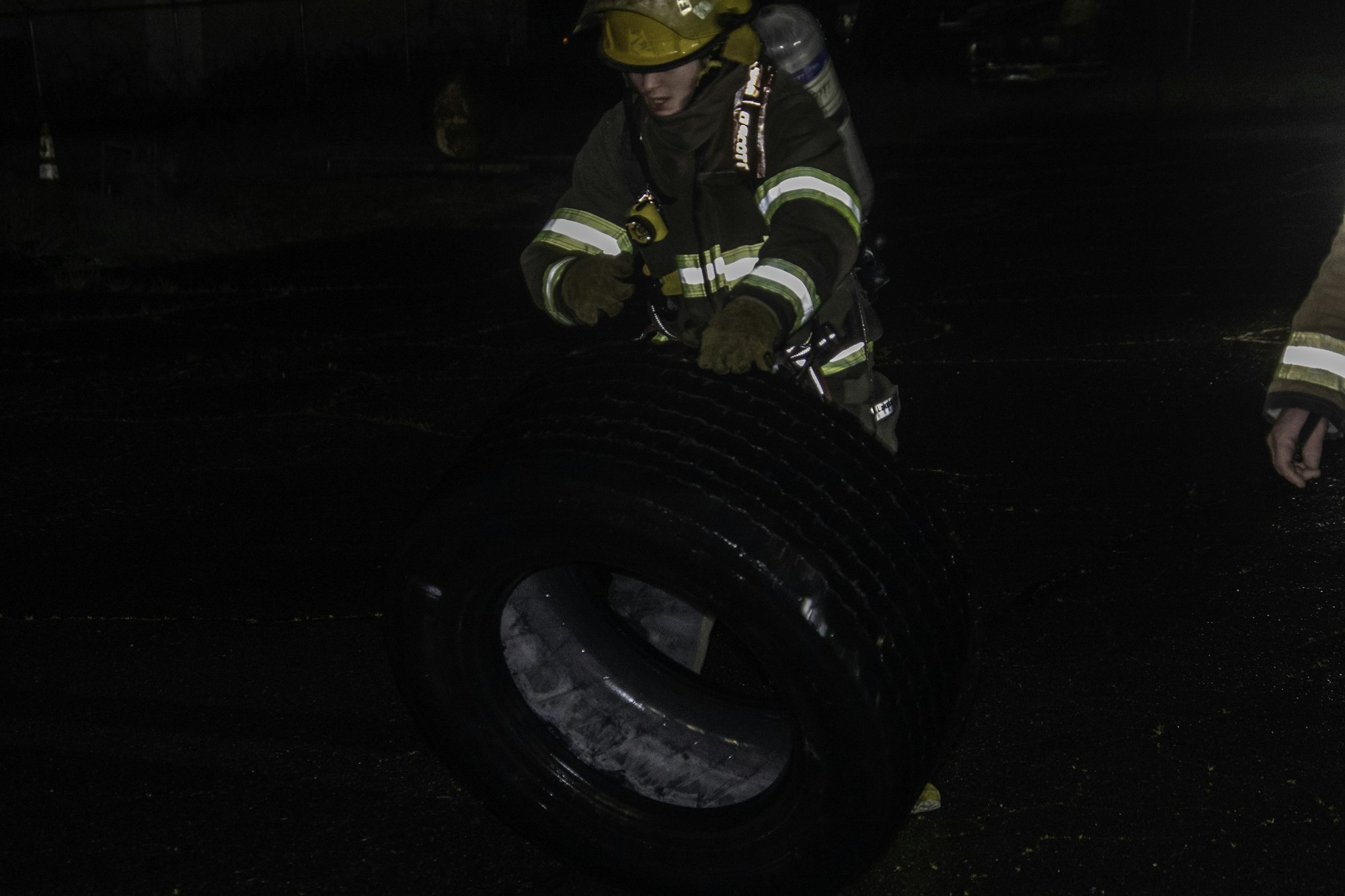 A firefighter handling a large tire in a dark, outdoor setting.
