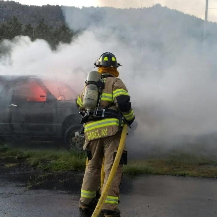 A firefighter with a hose near a smoking vehicle.