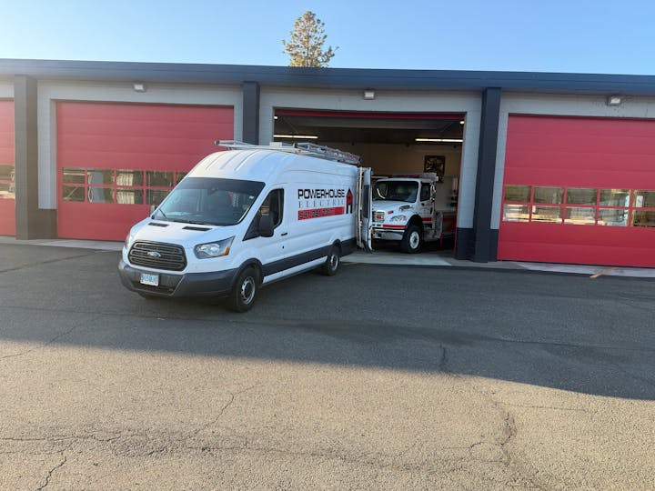 A white van labeled "Powerhouse Electric" is parked in front of a building with red garage doors.