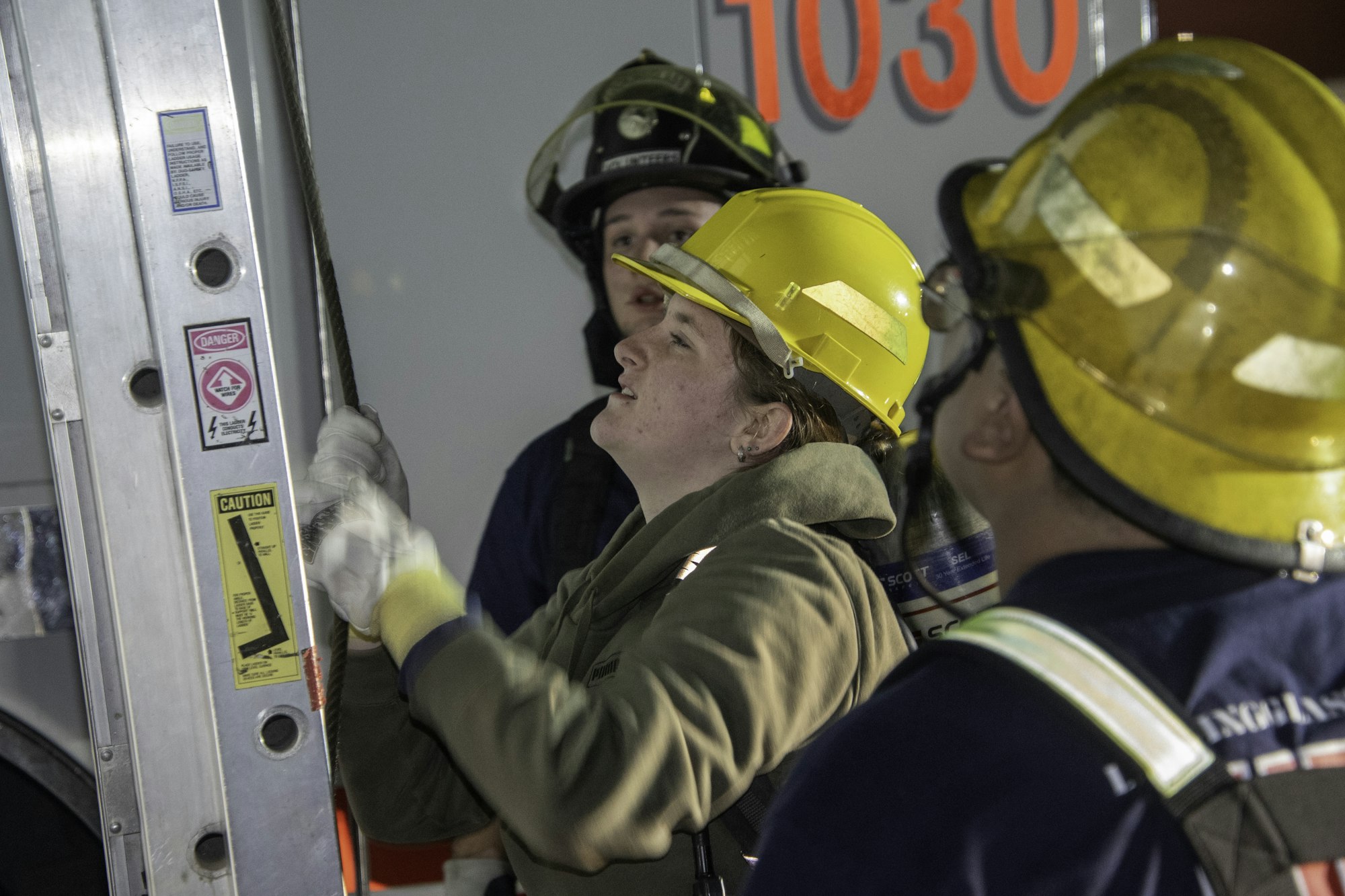 Firefighters in safety gear are working together, focusing on a task involving ropes and equipment. Their teamwork is evident.
