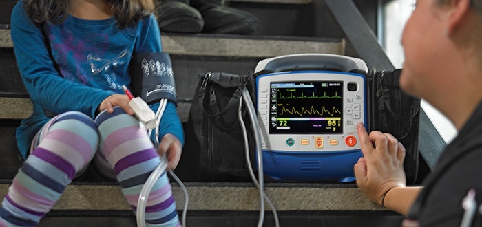 A child getting their vitals checked by a monitor while sitting on stairs, assisted by an adult.