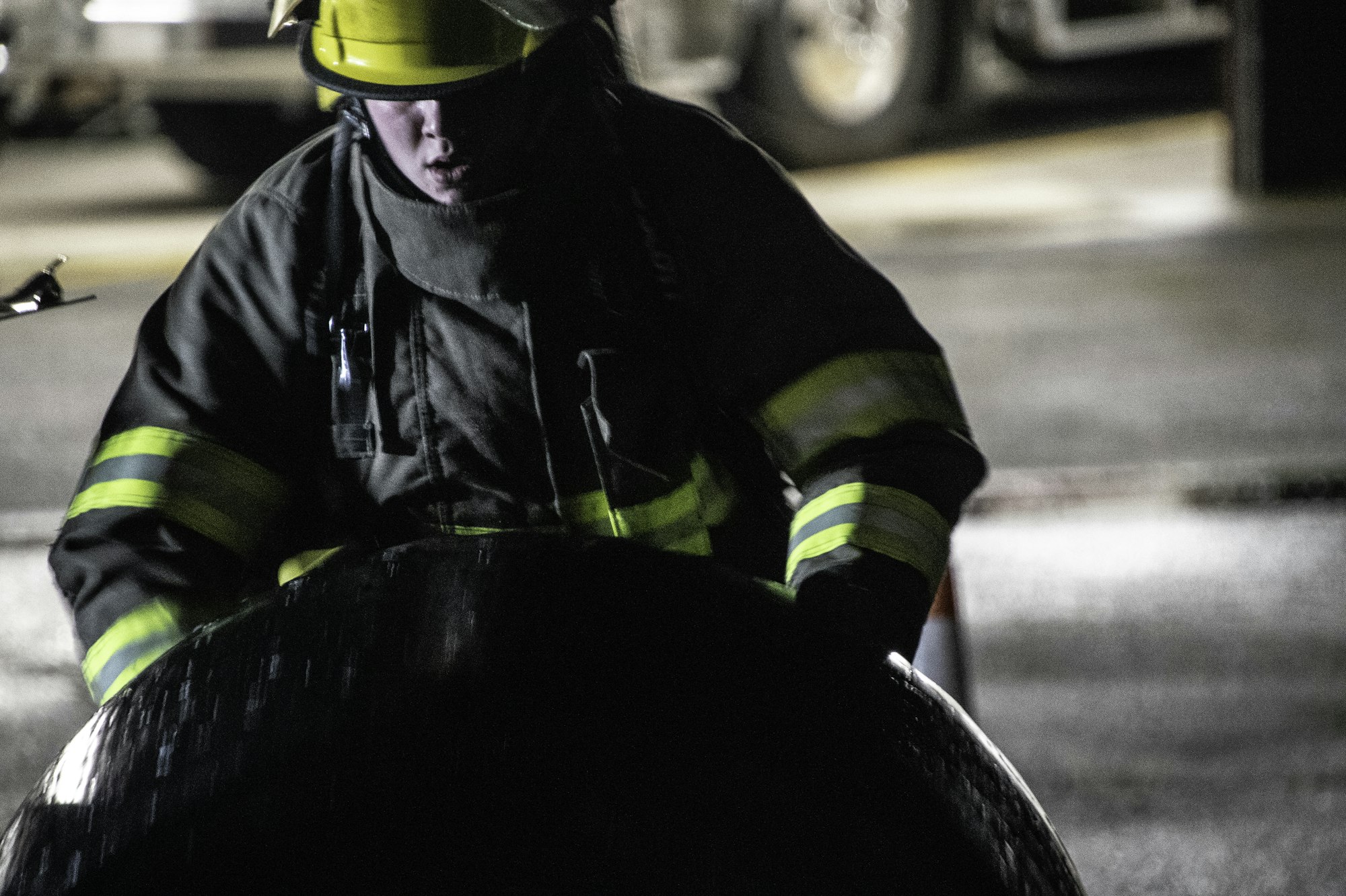 An individual in firefighting gear works with a large, dark object in a dimly lit environment. Safety and focus are key.