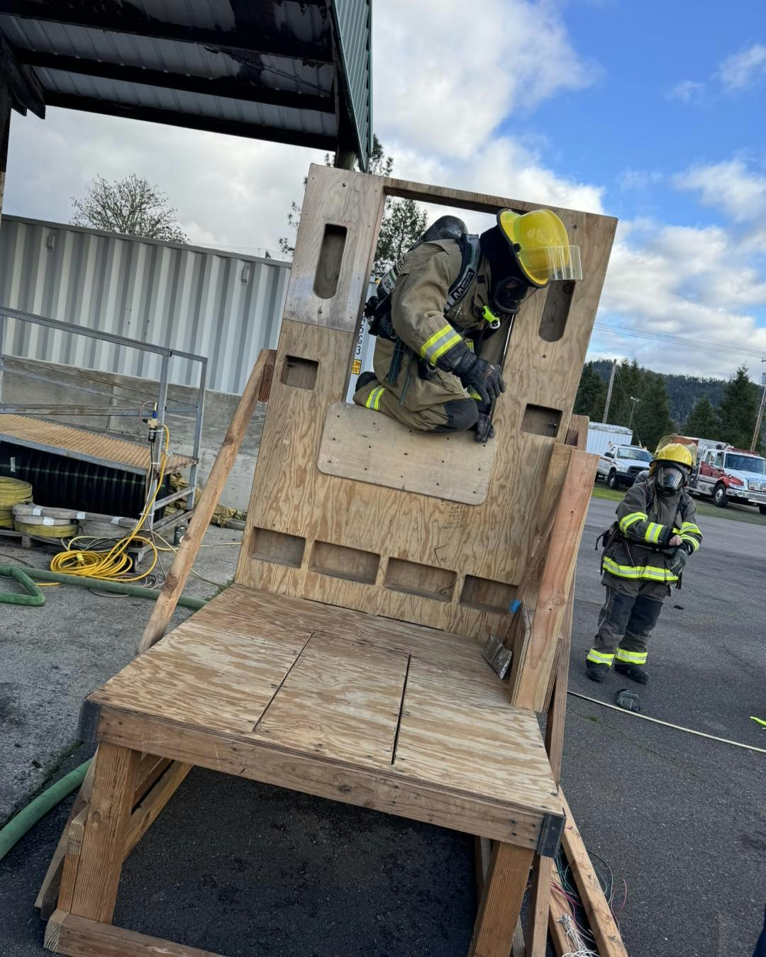 Firefighter in gear navigating a wooden obstacle course with another in the background.