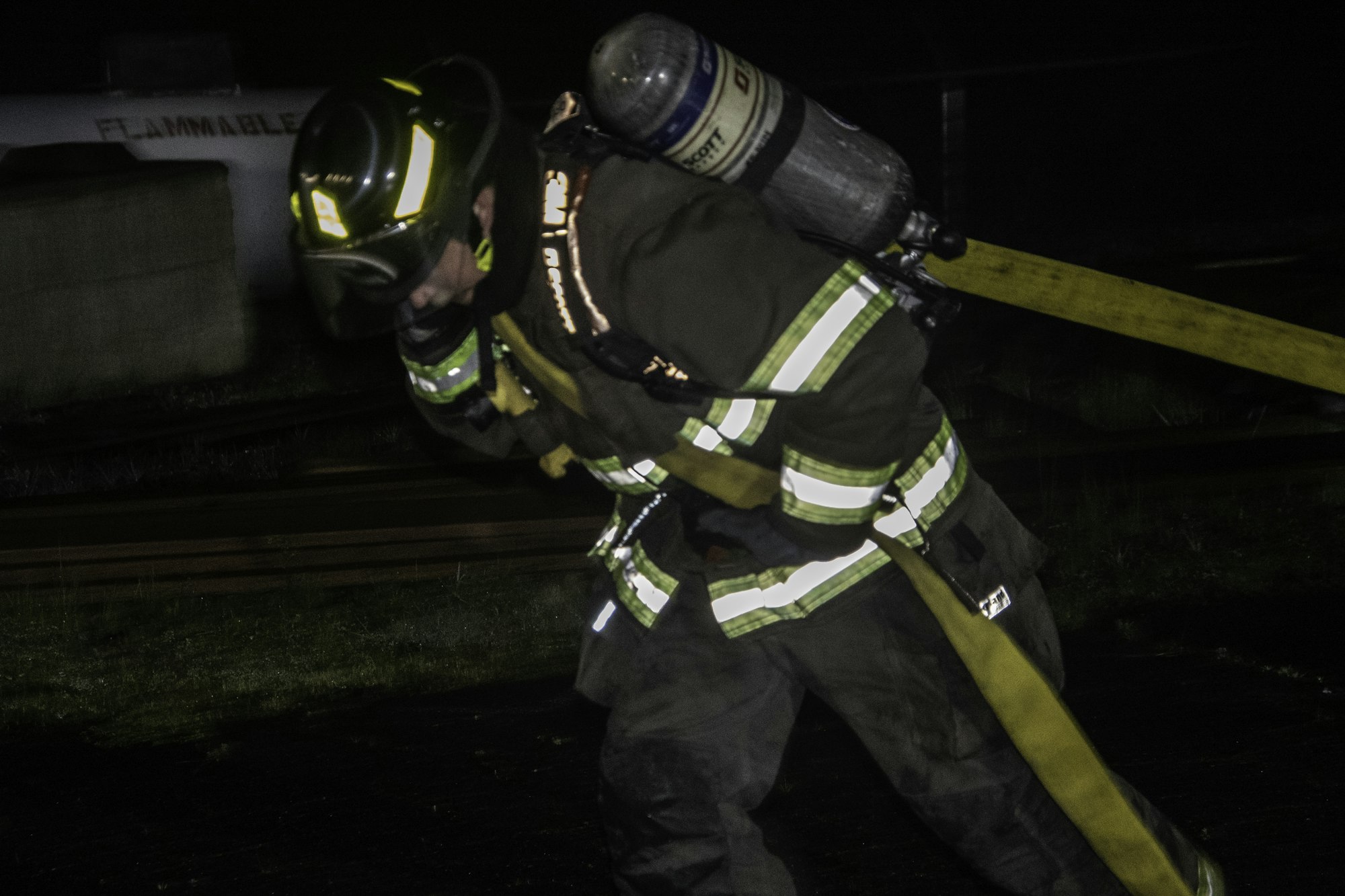 A firefighter in gear is carrying equipment at night, illustrating their readiness to respond to emergencies.