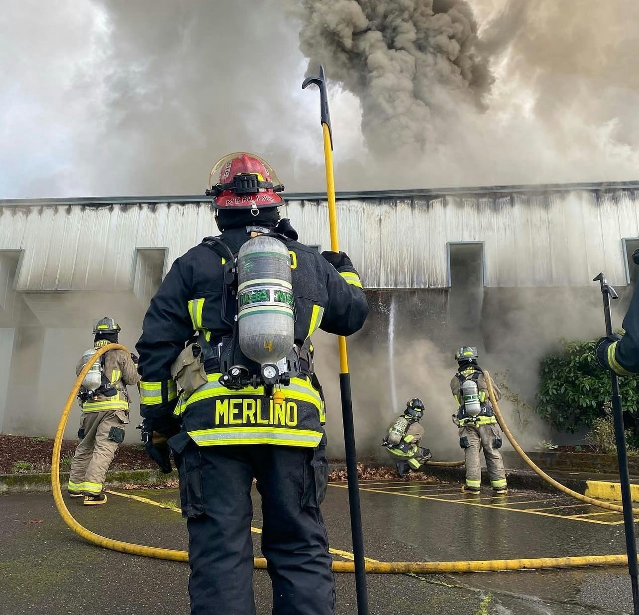 Firefighters battling smoke and fire outside a building with hoses and equipment.