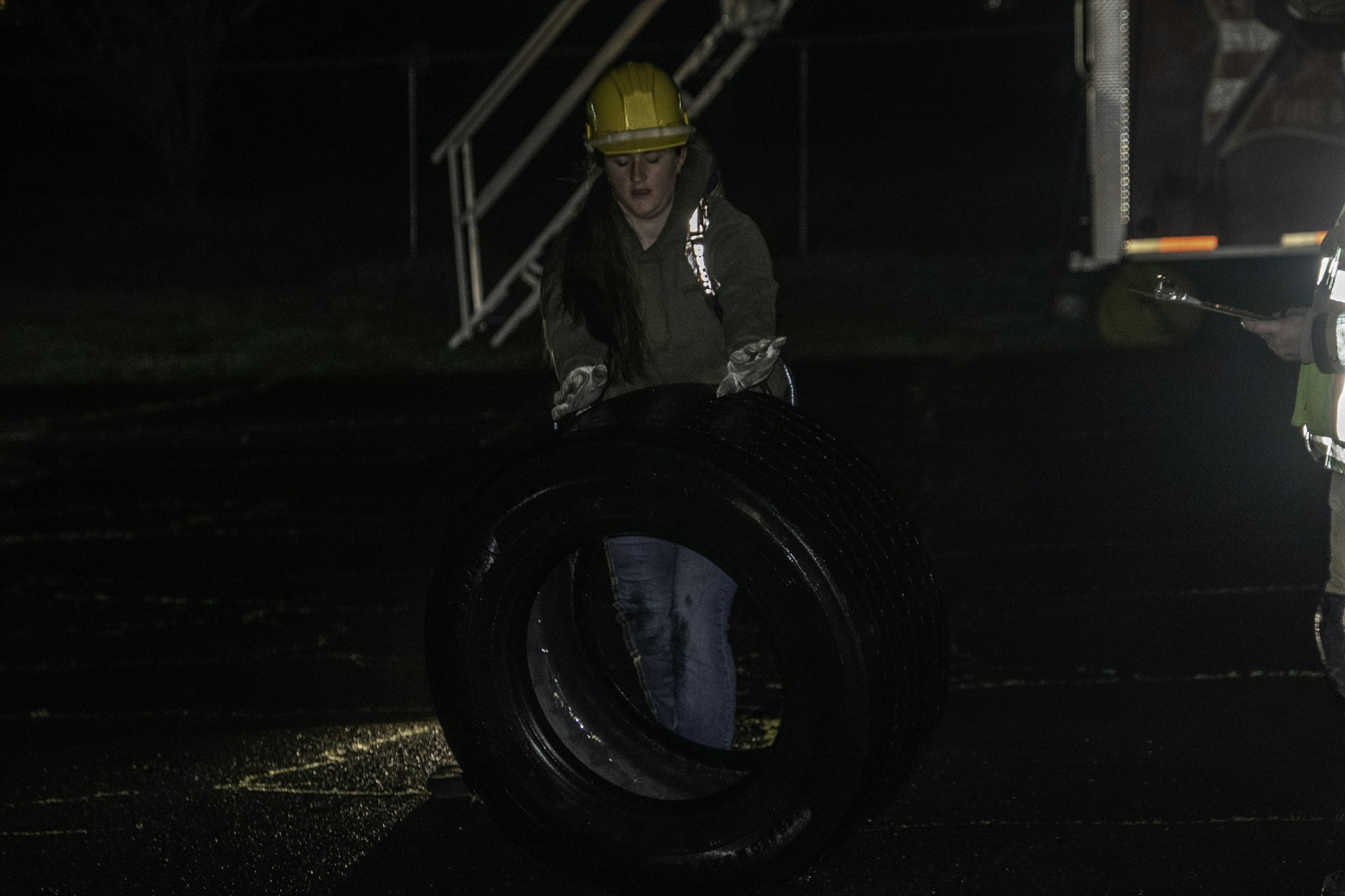 A person in a hard hat and gloves is lifting a tire in low light, possibly during a training or emergency response exercise.