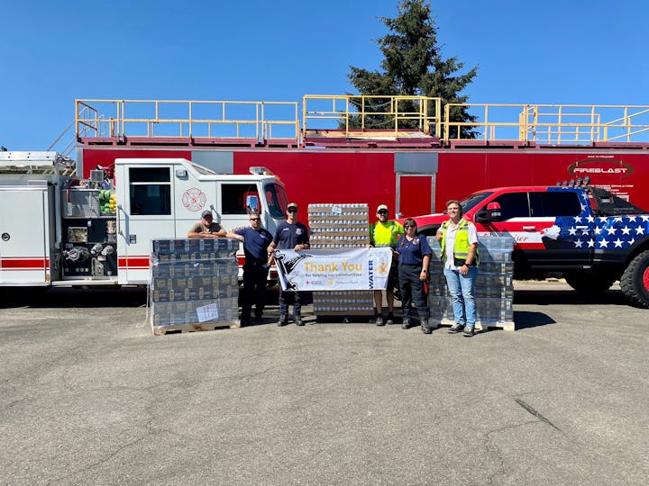 Firefighters and volunteers with water packs and a "Thank You" banner, in front of a fire engine and decorated truck.