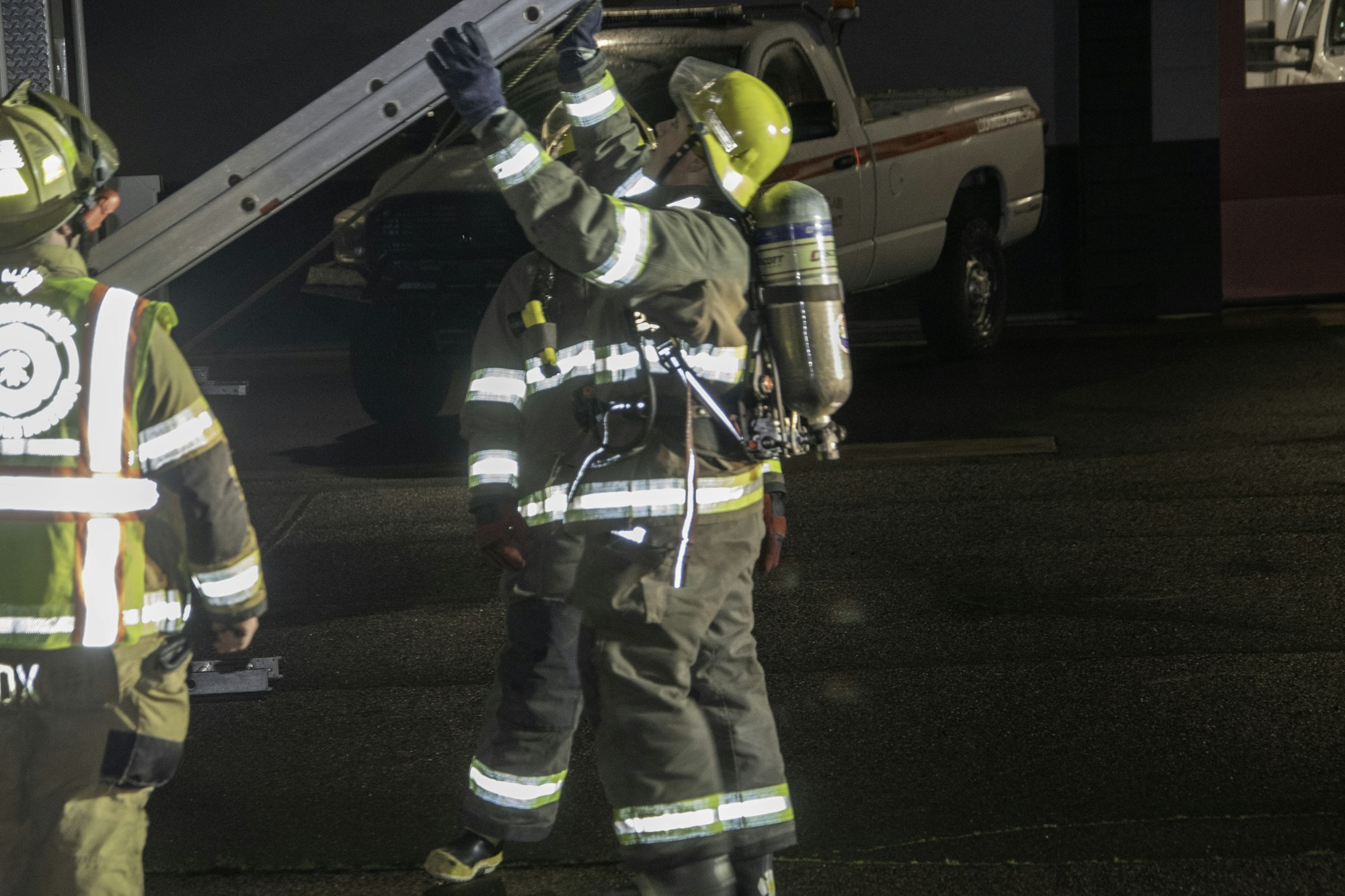 The image shows firefighters in protective gear, one using a ladder while another prepares for action.