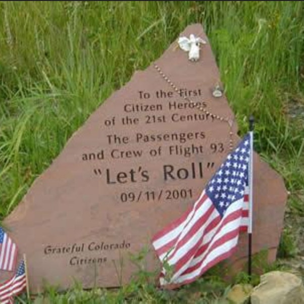 A memorial stone for Flight 93 passengers and crew, with flags and a rosary, honoring 9/11 heroes.