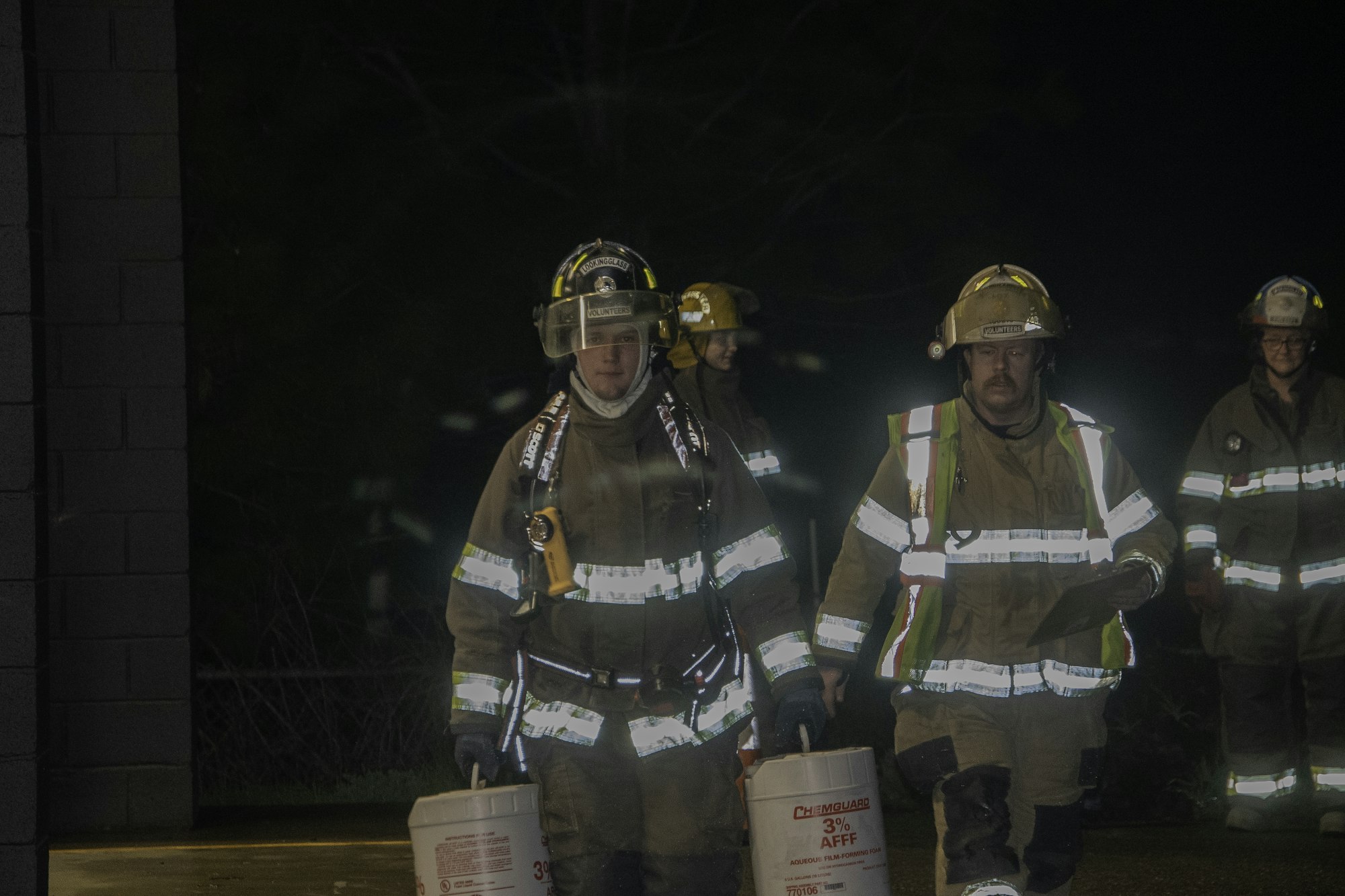 Firefighters in protective gear carry buckets at night, preparing for a response or training activity.