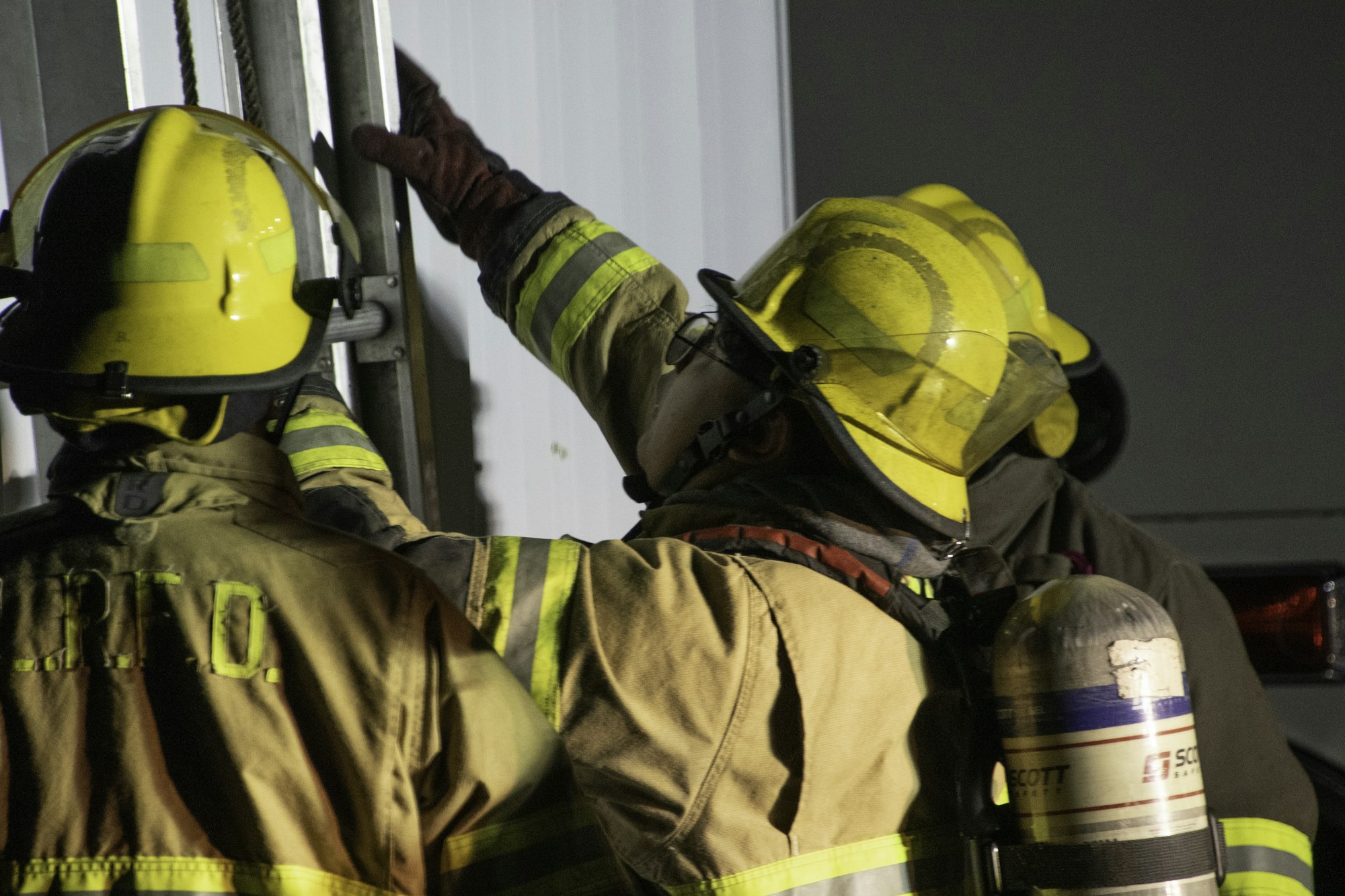 Three firefighters in helmets and gear are working together, possibly handling equipment or responding to an emergency.