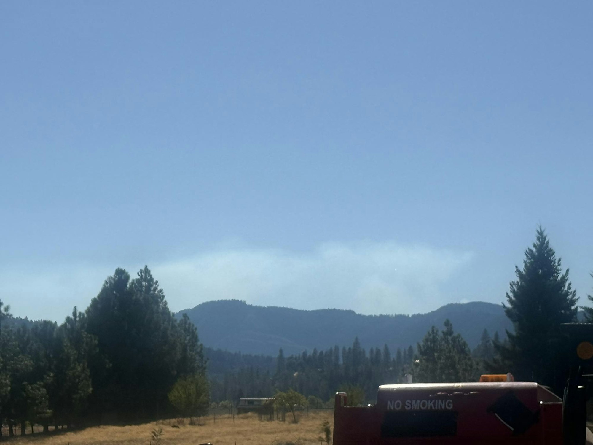 A scenic view of trees and mountains with a clear sky, and a "NO SMOKING" sign in the foreground.