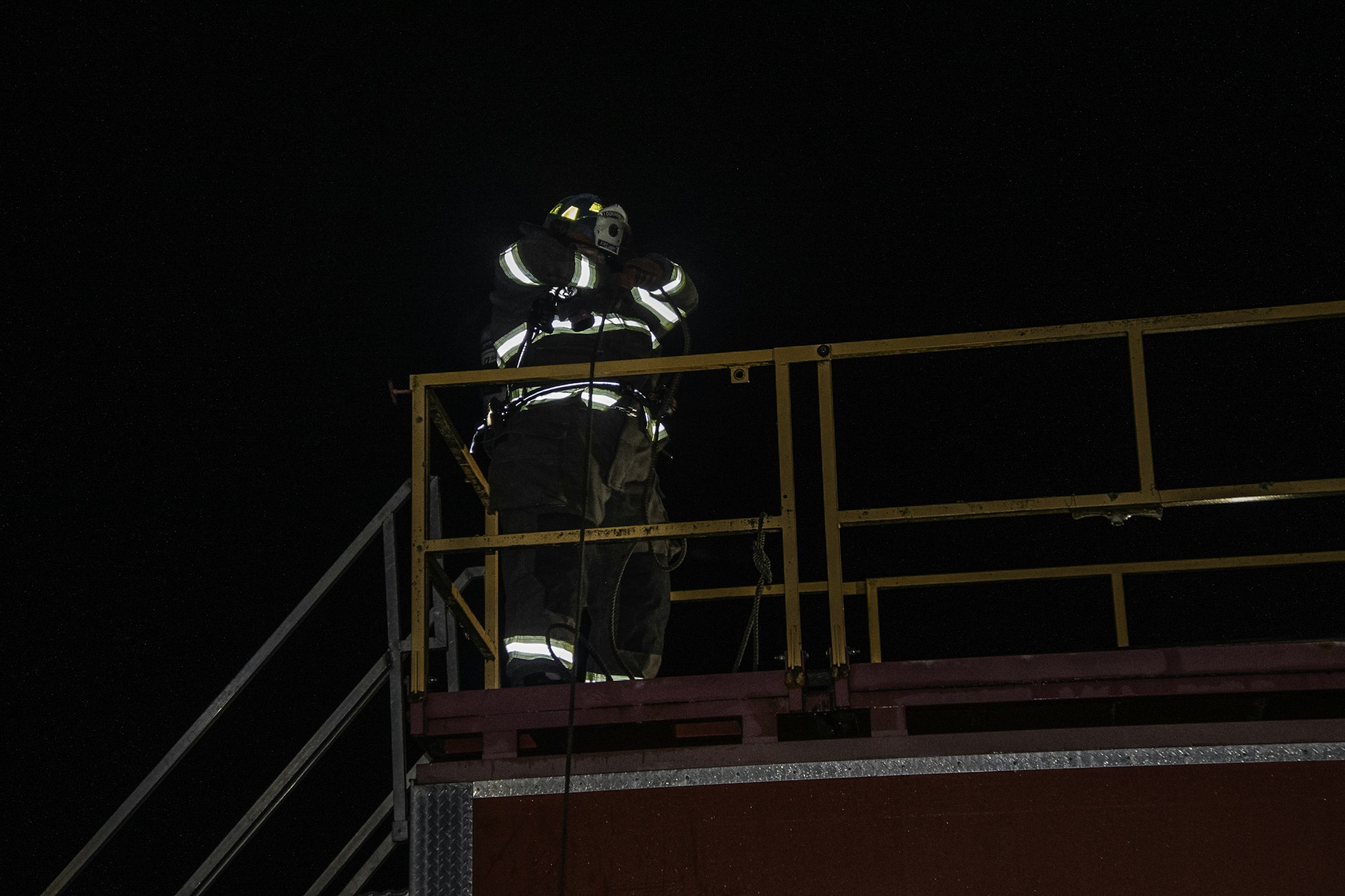 A firefighter in gear is positioned on a platform at night, possibly preparing for a task or observation.