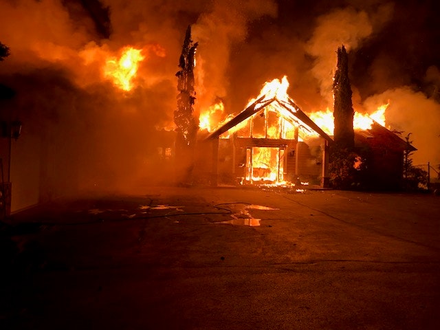 A house engulfed in flames at night, with intense fire and smoke rising into the sky.