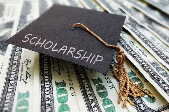 Graduation cap labeled "Scholarship" on top of stacked 100 dollar bills.