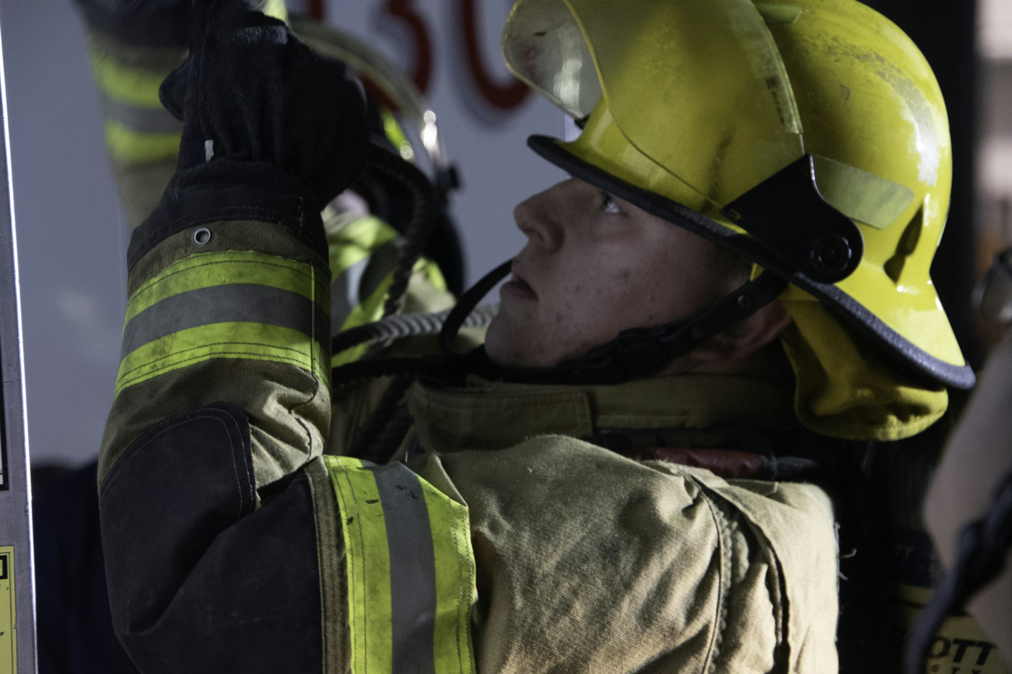 A firefighter in full gear, wearing a helmet, focuses intently while using equipment in a training or emergency scenario.